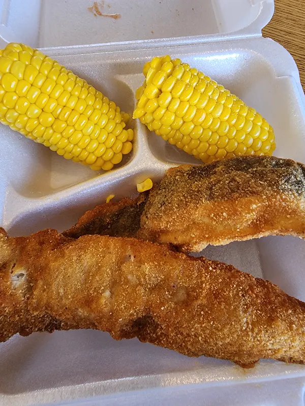 Cornmeal-fried fish fillets with two ears of corn in a takeout box