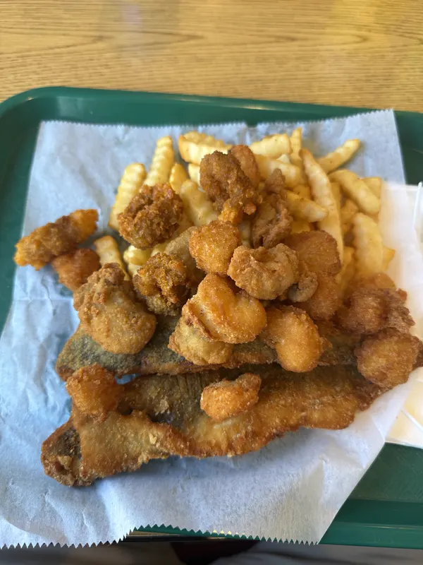 A fried seafood platter with fish, shrimp and scallops over crinkle fries on a green tray